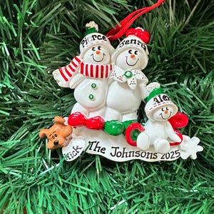 Puede incluir: Adorno navide&ntilde;o de una familia de mu&ntilde;ecos de nieve. El adorno presenta tres mu&ntilde;ecos de nieve con los nombres Pierce, Jenna y Alex en sus sombreros. La base dice "The Johnsons 2025" e incluye una peque&ntilde;a figura de perro.