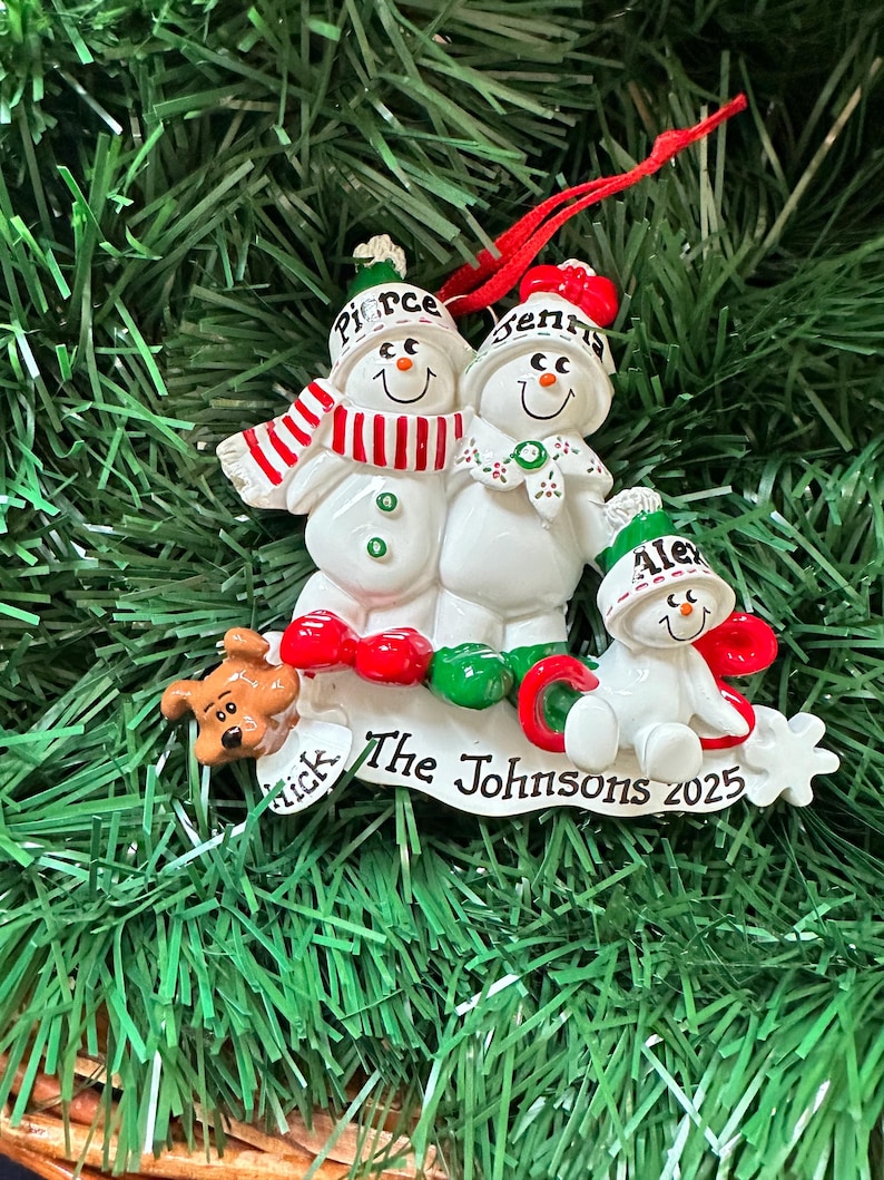 Puede incluir: Adorno navide&ntilde;o de una familia de mu&ntilde;ecos de nieve. El adorno presenta tres mu&ntilde;ecos de nieve con los nombres Pierce, Jenna y Alex en sus sombreros. La base dice "The Johnsons 2025" e incluye una peque&ntilde;a figura de perro.