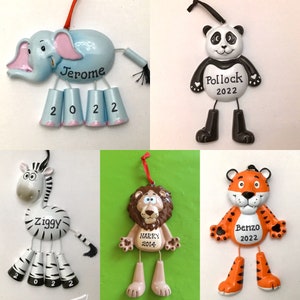 May include: Ten personalized Christmas ornaments featuring various animal designs. The ornaments are blue, black and white, brown, and orange. Each ornament has a name and year on it. The names are Jerome, Pollock, Ziggy, Harry, and Benzo. The years are 2022 and 2014.