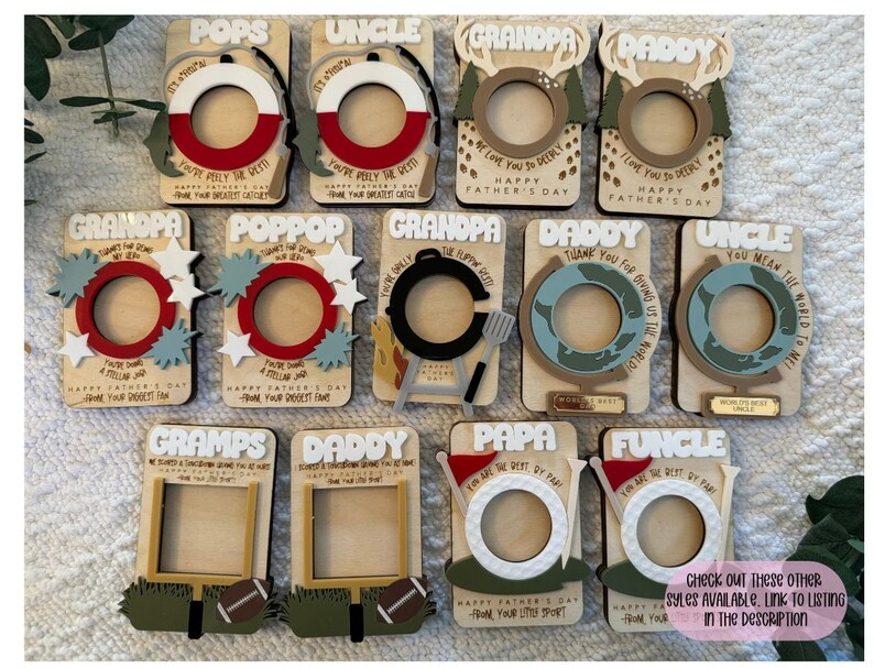 May include: A collection of wooden Father's Day photo frames with various designs and text. The frames feature words like "POPS", "UNCLE", "GRANDPA", and "DADDY". Each frame has a circular or rectangular opening for a photo, with decorative elements.