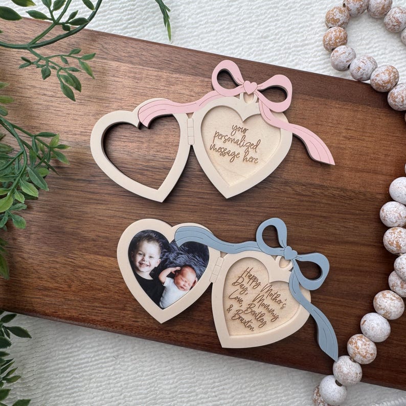 May include: Two heart-shaped wooden photo frames with attached bows. One frame has a pink bow and the text "your personalized message here." The other frame has a blue bow and a photo of two babies with the text "Happy Mother's Day, Mommy, Love, Bailey & Braxton."