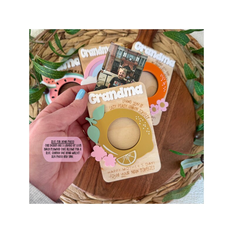 May include: Wooden photo frames with a lemon, watermelon, and rainbow design. The frames have a slot for a wallet-sized photo and the word "Grandma" on top. The lemon frame has the text "Happy Mother's Day!"