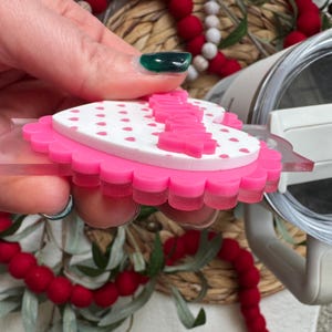 Op de afbeelding: Een roze en witte hartvormige decoratie met een geschulpte rand. De bovenste laag is wit met kleine roze hartjes en het woord "Happy" is roze uitgesneden. De decoratie wordt omhoog gehouden door een doorzichtig plastic stuk.