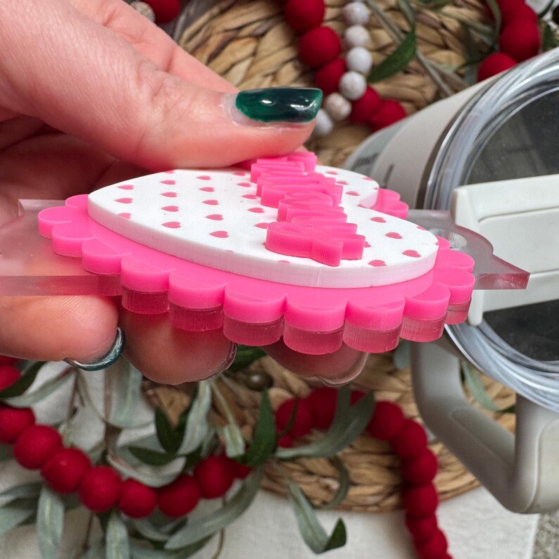 Op de afbeelding: Een roze en witte hartvormige decoratie met een geschulpte rand. De bovenste laag is wit met kleine roze hartjes en het woord "Happy" is roze uitgesneden. De decoratie wordt omhoog gehouden door een doorzichtig plastic stuk.