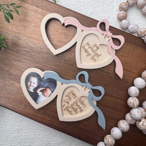 May include: Heart-shaped wooden photo frames with pink and blue ribbon accents. One frame displays a photo of two children, while another has the text "Happy Mother's Day, Love, Bentley & Braxton." The third frame has the text "your personalized message here."