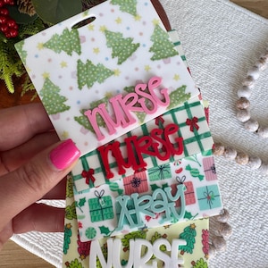 May include: Four rectangular acrylic badge reels featuring holiday patterns including green Christmas trees, red bows, and gift boxes. Each badge reel has a raised, colorful script or block letter word attached, reading nurse, nurse, xray, and nurse.