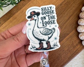May include: A white badge reel with a cartoon goose wearing a cowboy hat and boots. The text "SILLY GOOSE ON THE LOOSE" is printed above the goose. The badge reel has a clear plastic clip.