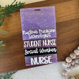 May include: A rectangular purple badge reel featuring four stacked sections with white text. The sections read Nuclear Medicine Technologist, STUDENT NURSE, Social Worker, and NURSE. The badge has a glittery finish and a top slot for attachment.