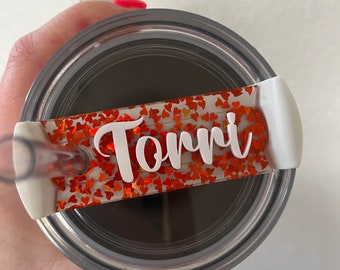 May include: A stainless steel tumbler with a white lid and a clear straw. The lid features a rectangular accent filled with orange heart-shaped confetti and the name "Torri" in white script.