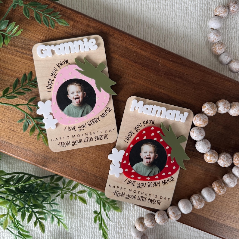 May include: Two wooden Mother's Day gifts with photos of a child. One says "Grannie" and the other says "Mamaw" in white letters. Each has a strawberry design with the text "I love you berry much!" and "Happy Mother's Day - From your little sweetie."