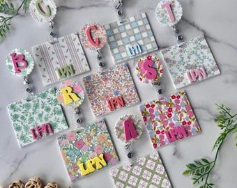 Puede incluir: Una colección de portatarjetas cuadrados con varios patrones florales y geométricos. Cada uno tiene un círculo festoneado con una letra y las letras LPN en un color contrastante sobre la base cuadrada del portatarjetas.
