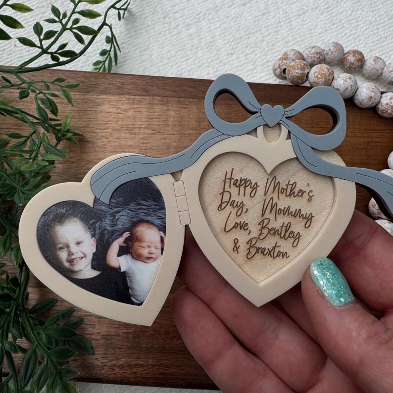 May include: A heart-shaped photo locket with a light blue bow and the words "Happy Mother's Day, Mommy Love, Bentley & Braxton" engraved inside. The locket opens to reveal two photos of children.