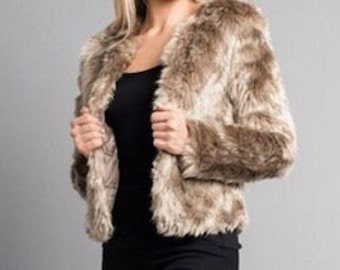 May include: A cropped faux fur jacket in shades of brown and tan. The jacket has long sleeves and a collarless design. The model is wearing a black top underneath. The jacket is open, revealing the black top.