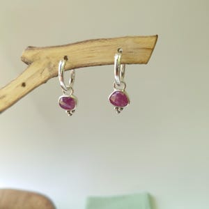 May include: A pair of silver hoop earrings with a pink gemstone dangling from each hoop.