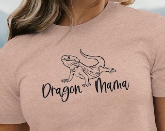May include: A light pink t-shirt with a black graphic of a bearded dragon and the text "Dragon Mama".