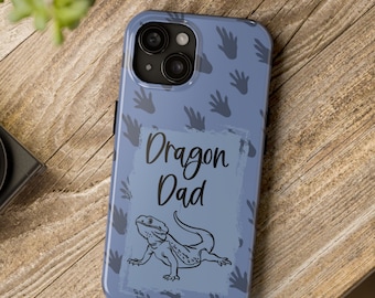 May include: A blue phone case with a pattern of black lizard footprints and the text "Dragon Dad". A black and white illustration of a bearded dragon is in the center of the case.
