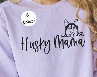 Può includere: Una felpa color lavanda con il testo "Husky Mama" in corsivo nero. Un cane husky bianco e nero sta guardando da sopra il testo. Un cerchio bianco con il testo "8 Colori" è nell'angolo in alto a sinistra dell'immagine.