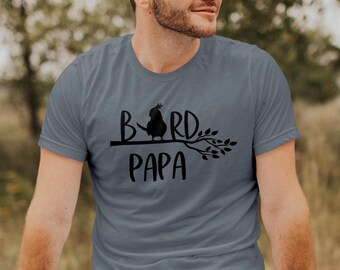 May include: A gray t-shirt with a black silhouette of a bird perched on a branch. The text "Bird Papa" is printed below the bird.