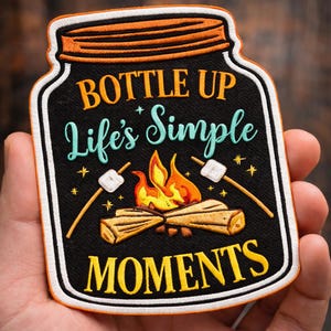 May include: Embroidered patch in the shape of a jar, with the words "Bottle Up Life's Simple Moments." The design includes a campfire with marshmallows on sticks. The jar has an orange lid and a black background.