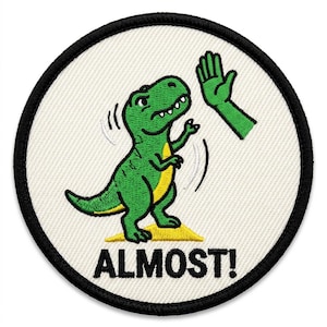 May include: Embroidered patch featuring a green dinosaur giving a high-five to a green hand. The dinosaur stands on a yellow platform, with the word "ALMOST!" in black below. The patch has a white background and a black border.