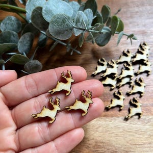 May include: Small wooden reindeer cutouts with a light brown finish. The reindeer are in a running pose and have detailed antlers. Several are scattered on a wooden surface, suggesting a craft or holiday theme.