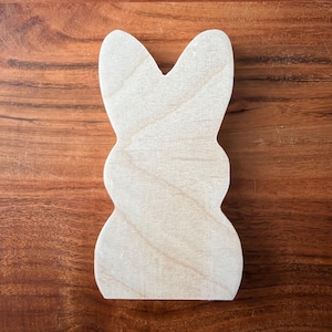 May include: A wooden bunny-shaped cutout with a natural wood grain finish. The cutout is light in color and has a smooth surface. The bunny shape is a classic Easter or spring craft item.