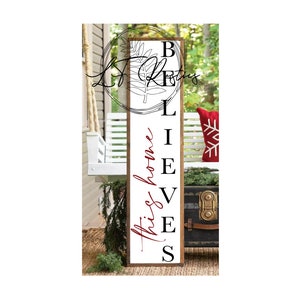 May include: A white wooden sign with the words "this home believes" written in black and red cursive. The sign is hanging on a porch with a white swing and a wooden chest.