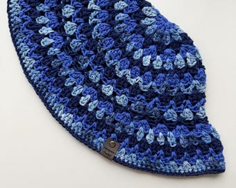 May include: A handmade crochet hat in shades of blue, from light to dark. The hat features a textured pattern and a small, brown tag with text. The hat is likely for sun protection or fashion.