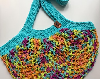 May include: A handmade crochet tote bag with a turquoise strap and top edge. The bag's body features a colorful open weave design in shades of orange, yellow, pink, and turquoise. A small brown leather tag is attached near the strap.