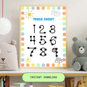 May include: A framed educational print with the words "TOUCH COUNT" and numbers 1 through 9. The numbers are black and have dots. The frame is light wood, and the background is white with colorful polka dots and cartoon illustrations.