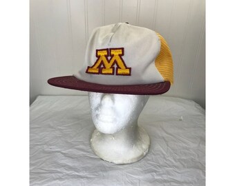 May include: A white and yellow trucker hat with a maroon brim. The hat has a large yellow "M" embroidered on the front.