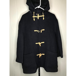 May include: A navy blue hooded duffel coat with wooden toggles and two front pockets. The coat is hanging on a white hanger against a white wall. The coat has a classic design.