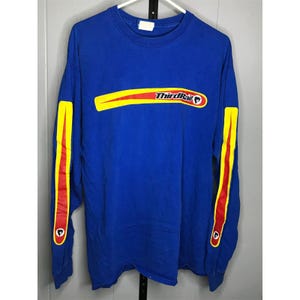 Puede incluir: Una camiseta de manga larga azul real con el texto "ThirdRail" en un diseño amarillo y rojo en el pecho. Las mangas tienen rayas amarillas y rojas con un pequeño logotipo cerca de los puños. La camiseta está colgada en una percha blanca.
