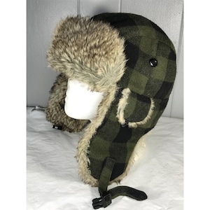 May include: A winter hat with a green and black plaid pattern. The hat has a faux fur lining and ear flaps. A black buckle is on the chin strap. The hat is designed to keep the head and ears warm in cold weather.