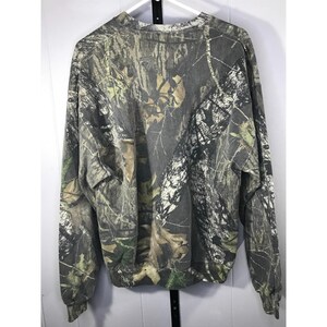 May include: A long-sleeved sweatshirt with a camouflage pattern in shades of green, brown, and gray. The crew neck sweatshirt is made of a soft material and is designed for casual wear. The pattern resembles a forest.