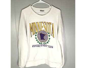 Puede incluir: Sudadera blanca con un estampado gráfico amarillo y morado del estado de Minnesota con el texto "Minnesota Established 1858".