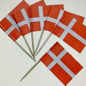 Könnte beinhalten: Eine Ansammlung kleiner dänischer Flaggen, jede mit einem weißen skandinavischen Kreuz auf rotem Grund. Die Flaggen sind an Holz-Zahnstochern befestigt, fächerförmig angeordnet und für dekorative Zwecke geeignet.
