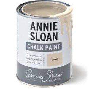 May include: A partially open can of Annie Sloan Chalk Paint in the color "Canvas." The can is cylindrical with a white label, gray accents, and the brand name prominently displayed. Paint drips down the side.