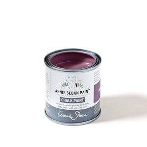 May include: A small, open can of Annie Sloan Chalk Paint in a muted purple hue. The can is silver with a white label featuring the brand name and product details. The label includes the text "CHALK PAINT" and "Annie Sloan Paint".