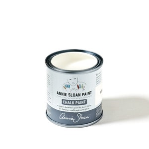 May include: A white can of Annie Sloan Chalk Paint. The can has a label with a drawing of a person with colorful hands and the text "Annie Sloan Paint Chalk Paint" and "a unique decorative paint by Annie Sloan for furniture, walls and paint effects".