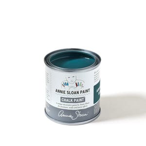 May include: A small, open can of Annie Sloan Chalk Paint in a teal color. The can has a white label with the brand name and product details. The label features a drawing of a person with colorful hands. The paint is for furniture, walls, and paint effects.