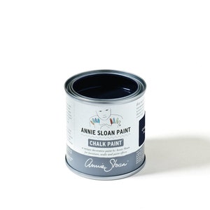 May include: A can of Annie Sloan Chalk Paint in the color Old Violet. The paint is a dark blue color and the can has a white label with the Annie Sloan logo and the words "Chalk Paint" and "Old Violet".