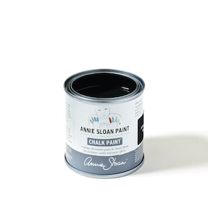 May include: A can of Annie Sloan Chalk Paint in the color Athenian Black. The can is silver with a black label and a cartoon illustration of a person with painted fingers.