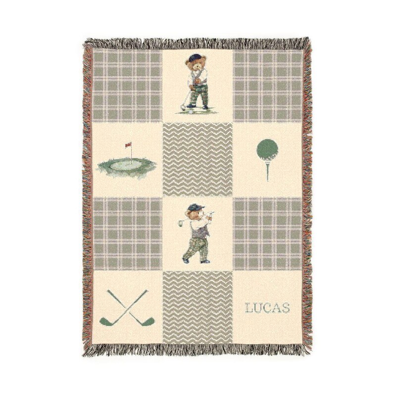 May include: A beige and green golf-themed throw blanket with a plaid pattern and fringe trim. The blanket features illustrations of a bear playing golf, a golf course, golf ball on a tee, and crossed golf clubs. The name "LUCAS" is printed on the blanket.