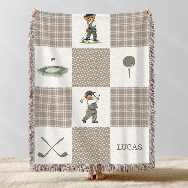 May include: A beige and white throw blanket with a golf theme. The blanket features a plaid pattern, golf-related illustrations, and a personalized name. The illustrations include a golf ball, golf clubs, and a bear playing golf.