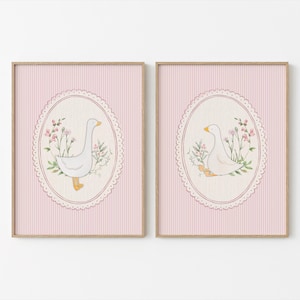 Puede incluir: Dos impresiones enmarcadas con ilustraciones en acuarela de gansos blancos con picos y patas amarillas, rodeados de flores rosas y vegetación. La obra de arte está sobre un fondo a rayas rosas dentro de un marco ovalado.