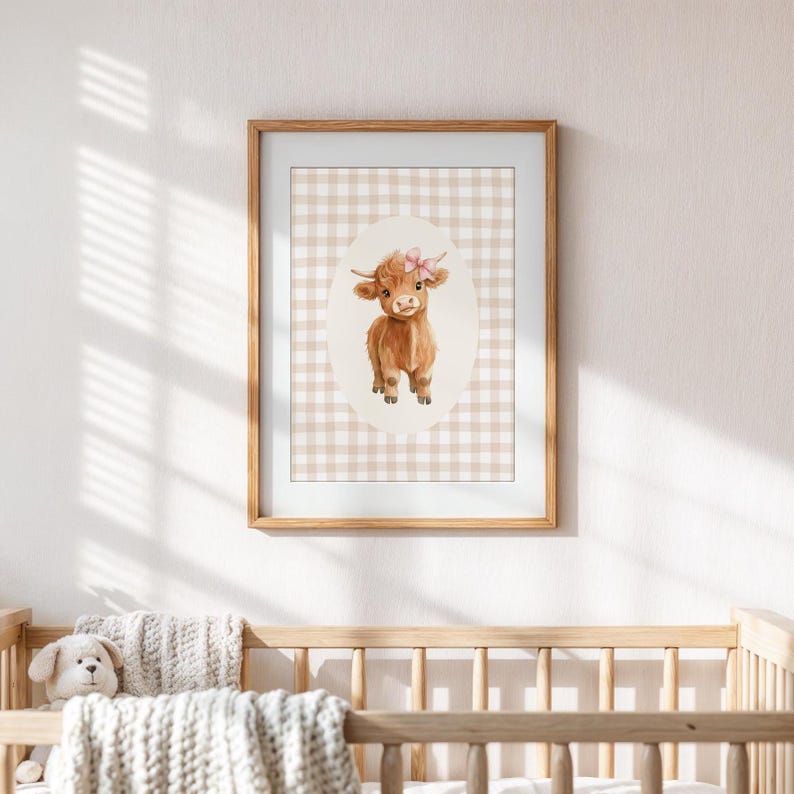 May include: A framed print of a watercolor illustration of a brown Highland cow with a pink bow on its head. The cow is standing on a white and brown gingham background.