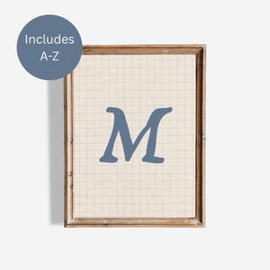 May include: Framed print featuring the letter "M" in a muted blue hue. The letter is centered on a grid-patterned background, encased in a wooden frame. A blue circle in the upper left corner reads "Includes A-Z".