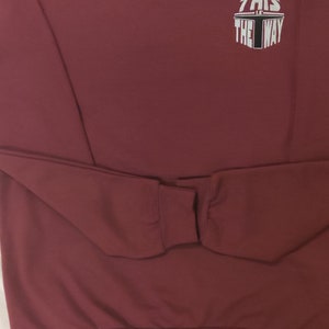 Puede incluir: Sudadera color burdeos con un gr&aacute;fico blanco que dice "This is the way" en un dise&ntilde;o circular.