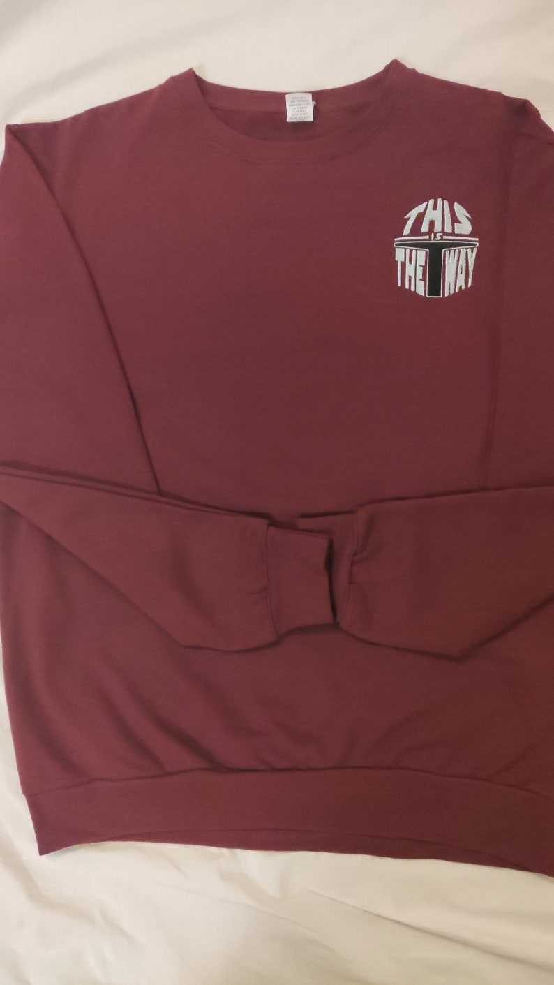 Puede incluir: Sudadera color burdeos con un gr&aacute;fico blanco que dice "This is the way" en un dise&ntilde;o circular.